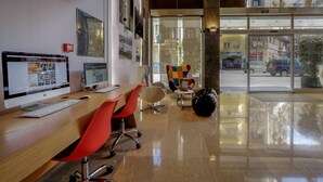 A modern hotel lobby with a wooden reception desk, a computer, and red office chairs.