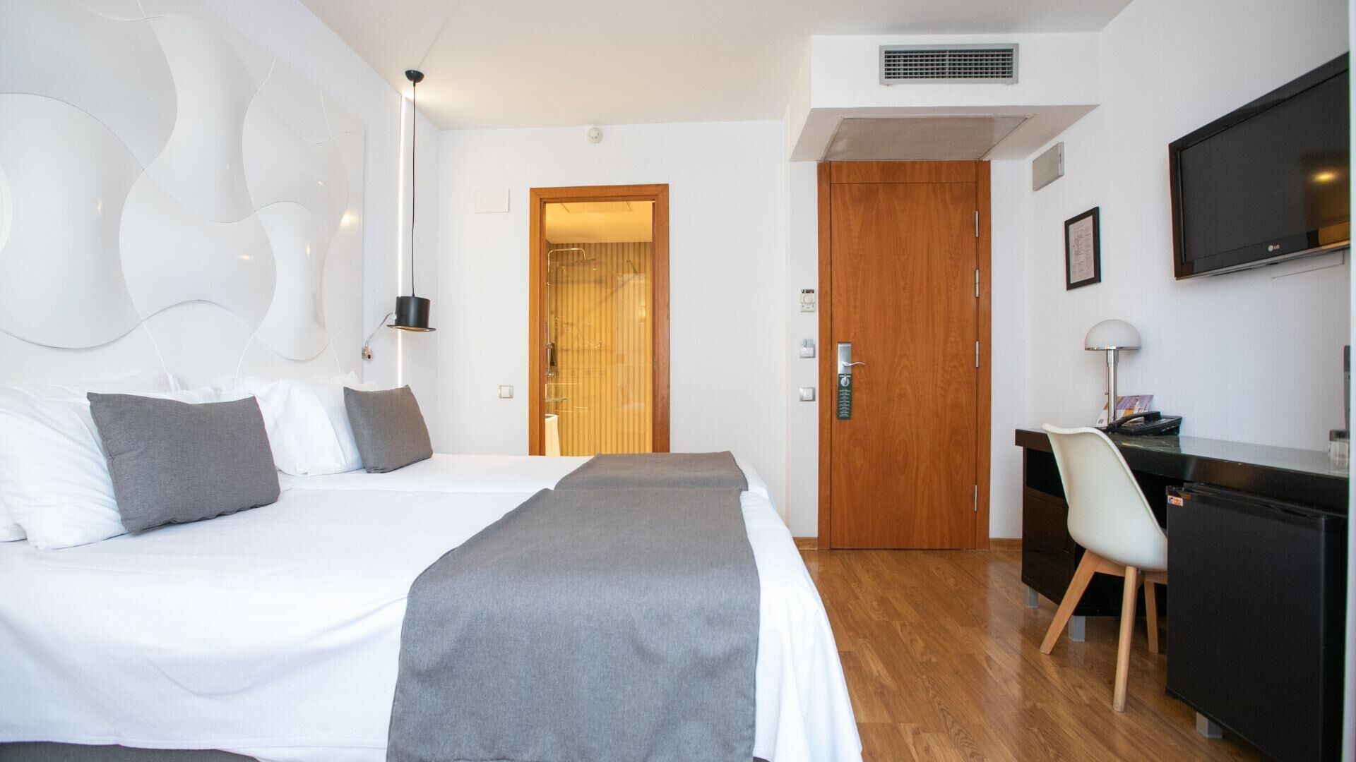A hotel room with a large bed, a desk, a chair, and a television.