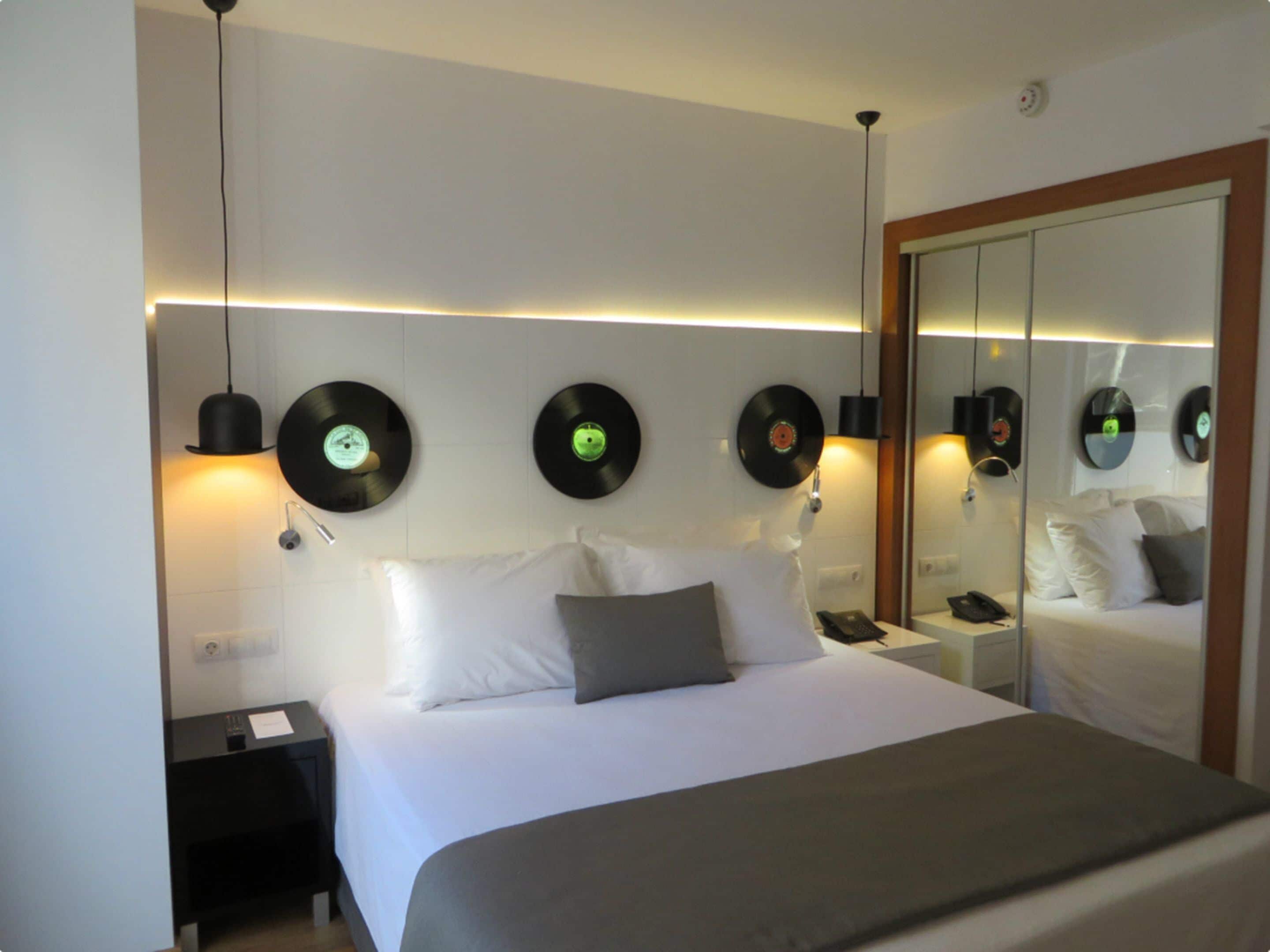 A hotel room with a bed, bedside tables, a mirror, and wall-mounted record players.
