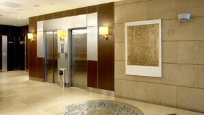 A modern elevator area with a marble floor, a wall-mounted artwork, and a light fixture. - Evenia Rocafort (Barcelona)