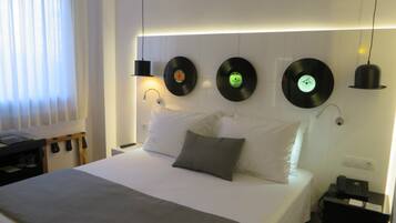 Una habitación de hotel moderna con una cama bien tendida, una mesita de noche con lámpara y tocadiscos montados en la pared.