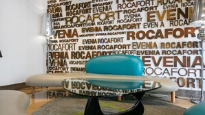 A modern interior with a word cloud wall, a glass table, and a blue chair. - Evenia Rocafort (Barcelona)