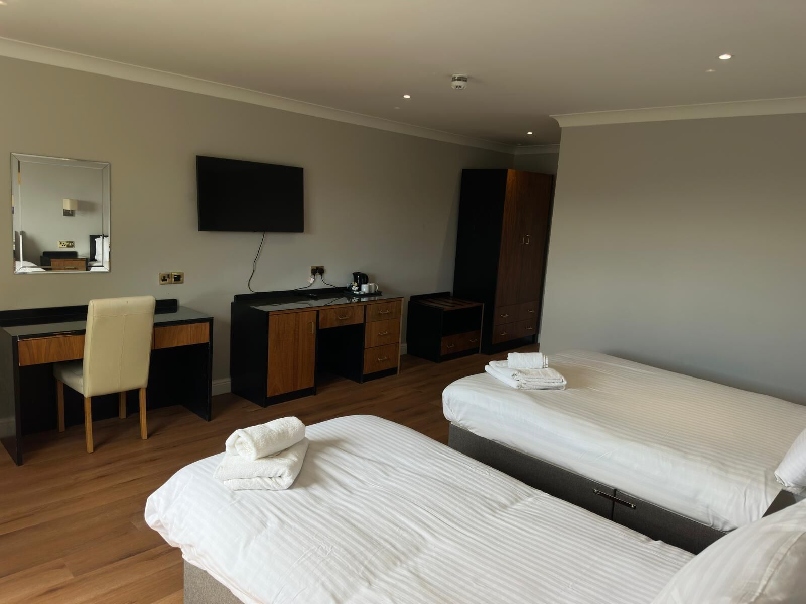 A hotel room with two beds, a desk, a chair, a wardrobe, and a TV.