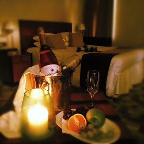 A bottle of champagne in a bucket, a lit candle, a glass, and a plate with fruit on a table in a hotel room. - Staindrop Hotel (Sheffield)