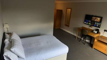 Ein Hotelzimmer mit Bett, Schreibtisch, Stuhl, Fernseher und Spiegel.