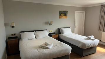 A hotel room with two beds, a painting on the wall, a door, and a window with curtains.