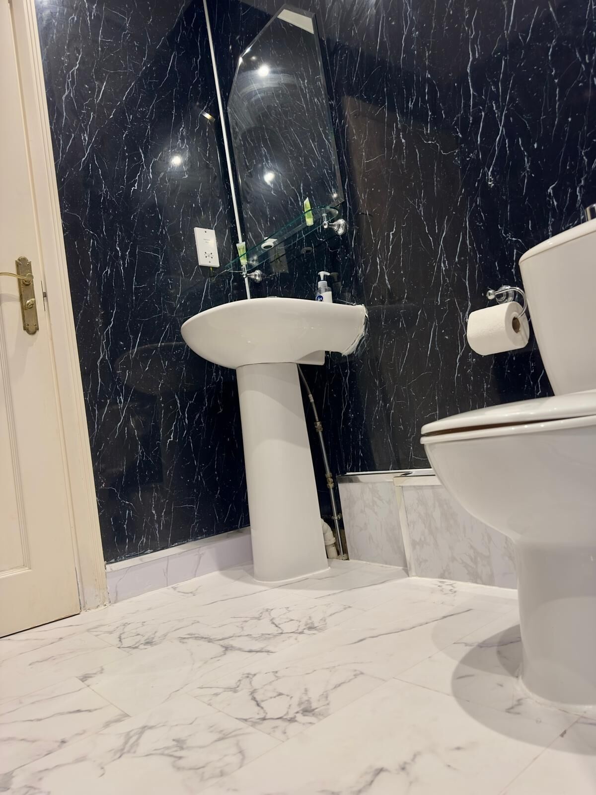 Une salle de bain avec un lavabo blanc, des toilettes et un sol en marbre.