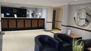 A hotel reception area with a reception desk, a clock, a sign indicating a 24-hour service, and a reception counter. - Staindrop Hotel (Sheffield)