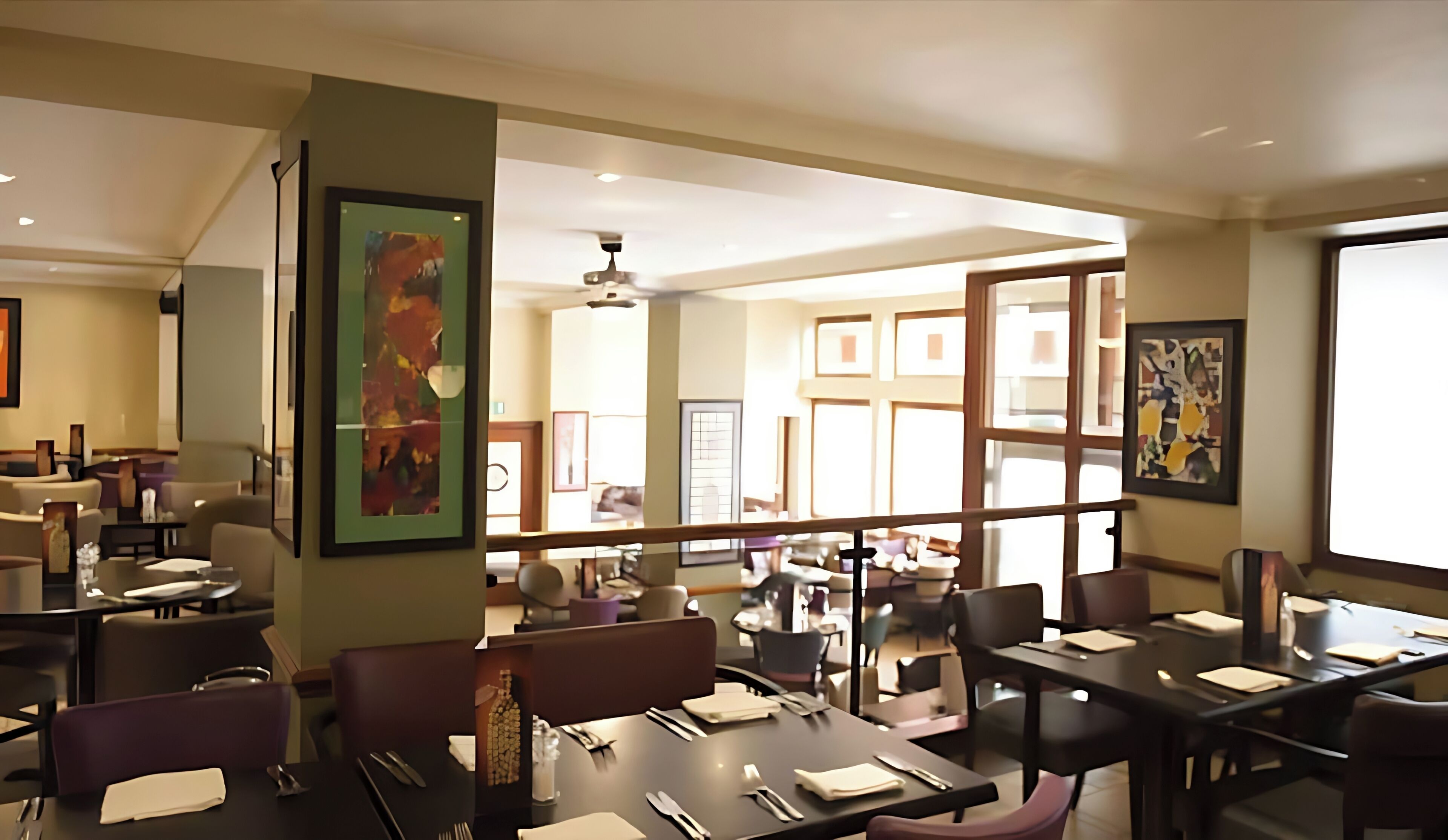 Un comedor moderno con varias mesas y sillas, obras de arte en las paredes y vistas a la habitación contigua.