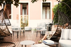 An outdoor seating area with cushioned chairs and tables, a wooden deck, and a building with large windows in the background.