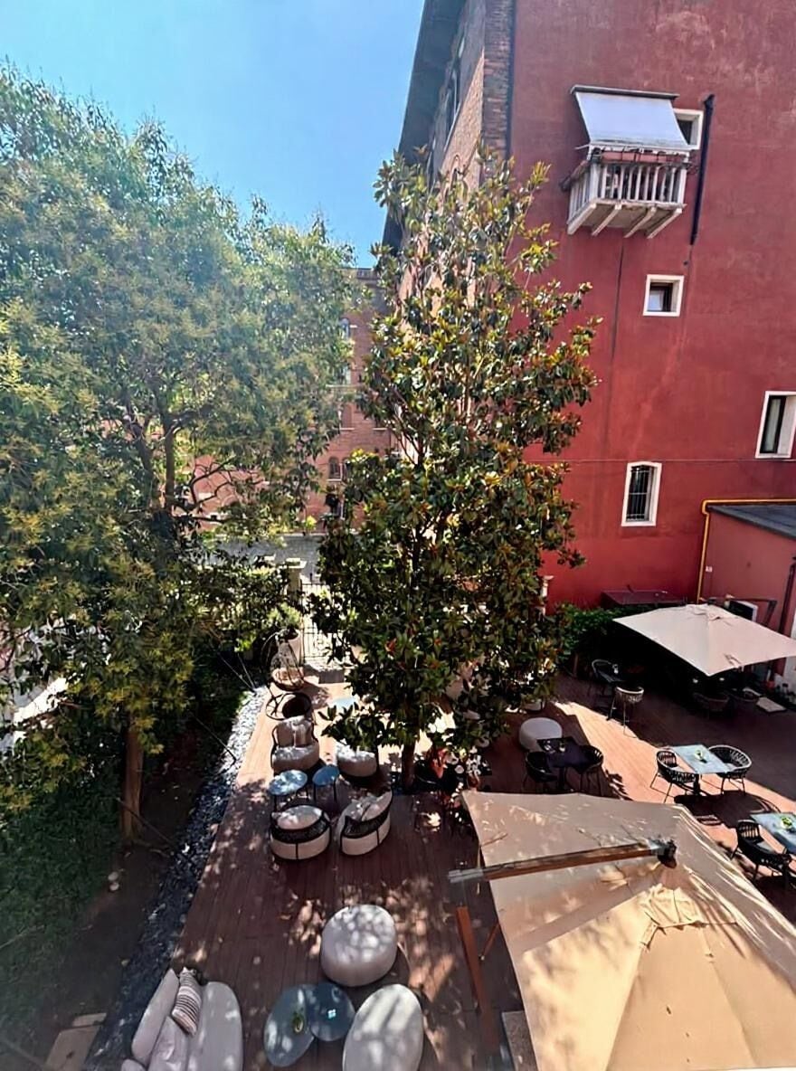 Un patio con mobiliario exterior, un árbol y un edificio rojo.