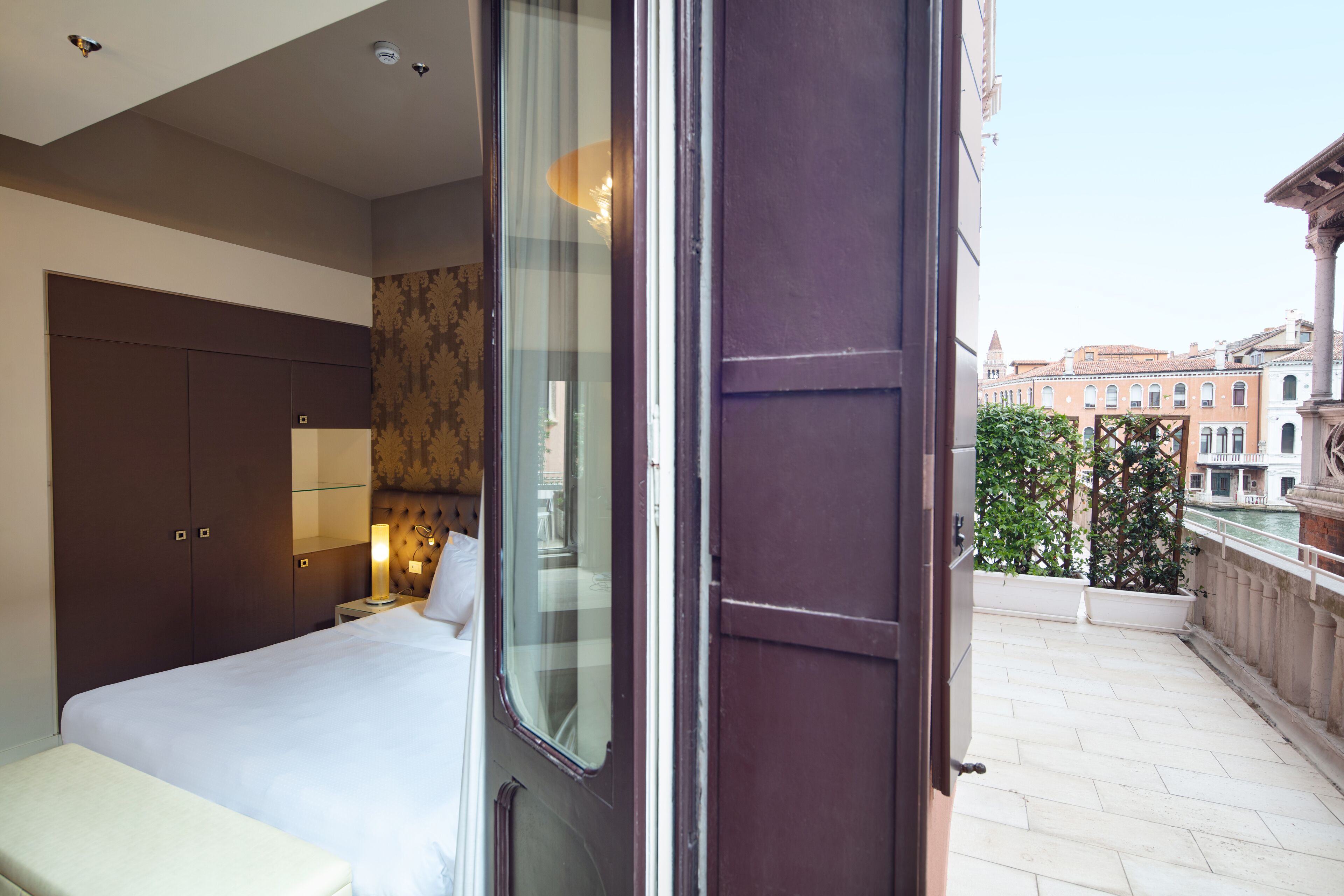 A hotel room with a bed, a wardrobe, a nightstand, and a view of the cityscape.
