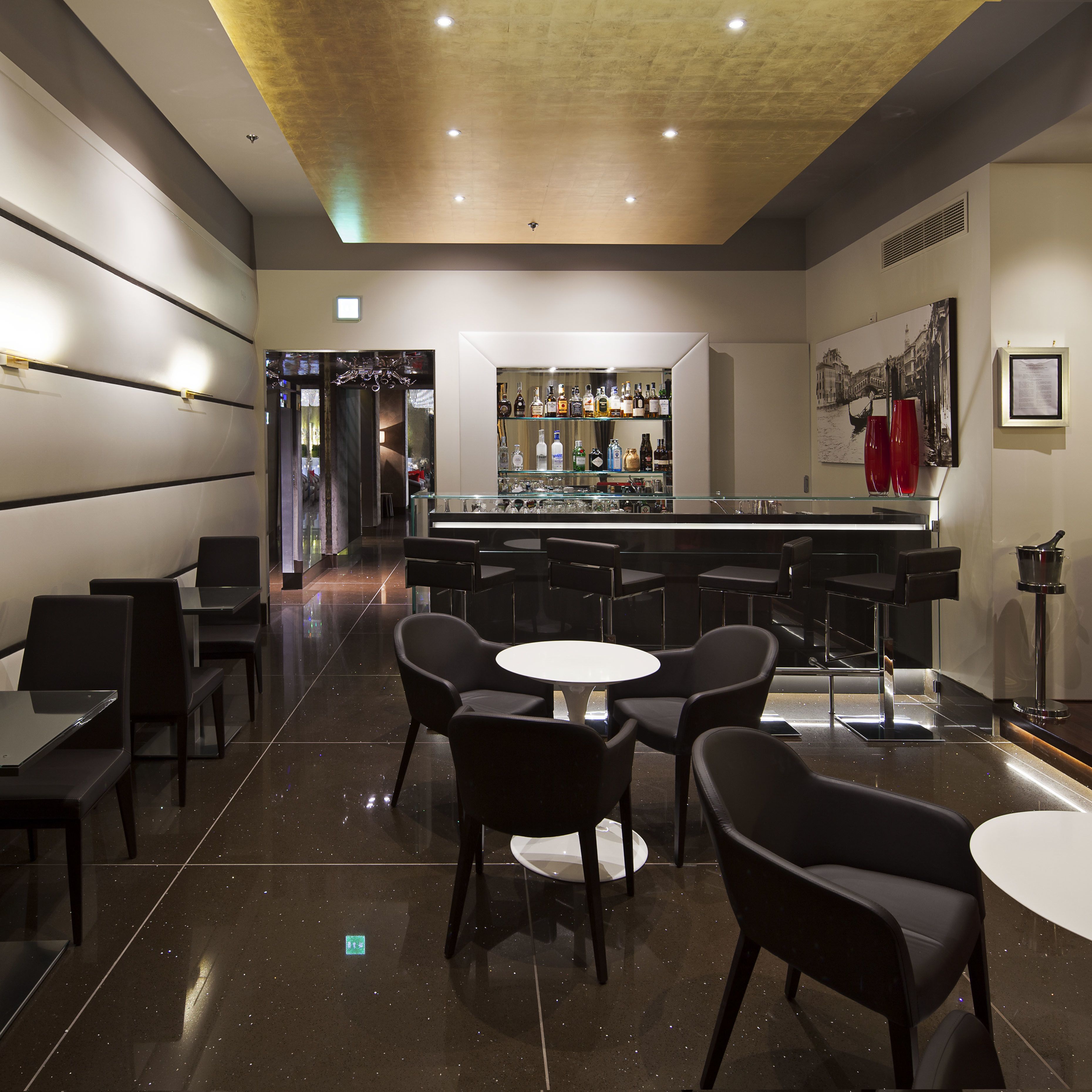 Eine moderne Bar mit glänzendem Boden, schwarzen Barhocker und einer Bartheke mit Glasplatte.