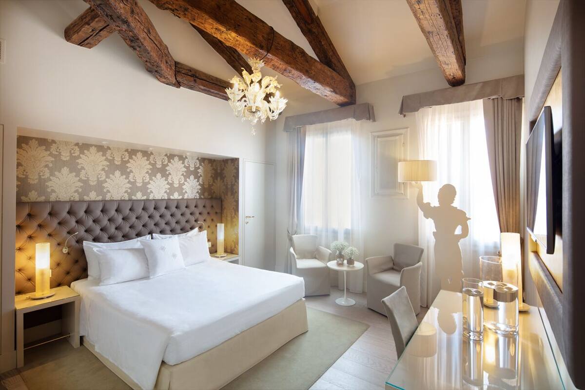 A hotel room with a large bed, a chandelier, a TV, and a seating area with a table and chairs.