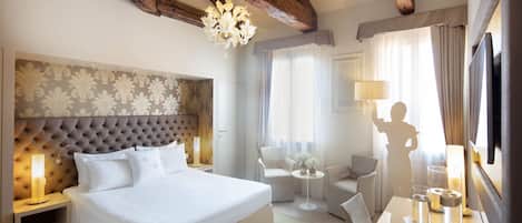 A hotel room with a large bed, a chandelier, a TV, and a seating area with a table and chairs.