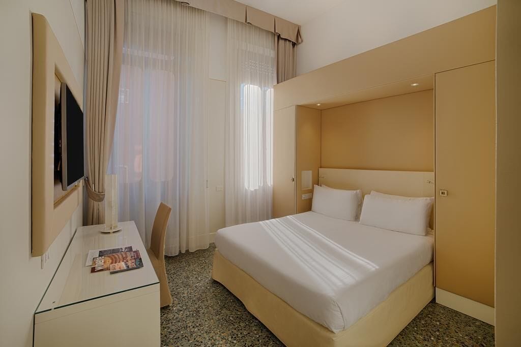 Una habitación de hotel con una cama, un escritorio, una silla, un televisor y cortinas.