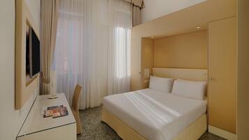 Una habitación de hotel con una cama, un escritorio, una silla, un televisor y cortinas.