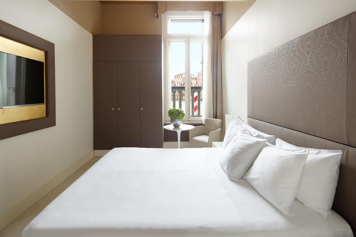 Una camera d'albergo con un letto grande, una TV a parete, un tavolino rotondo e vista sulla città attraverso una finestra.
