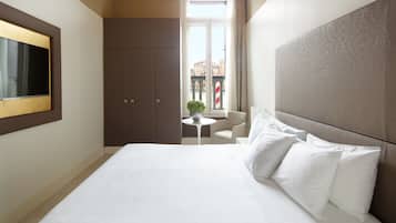 Habitación de hotel con una cama grande, un televisor montado en la pared, una pequeña mesa redonda y vistas a la ciudad a través de una ventana.