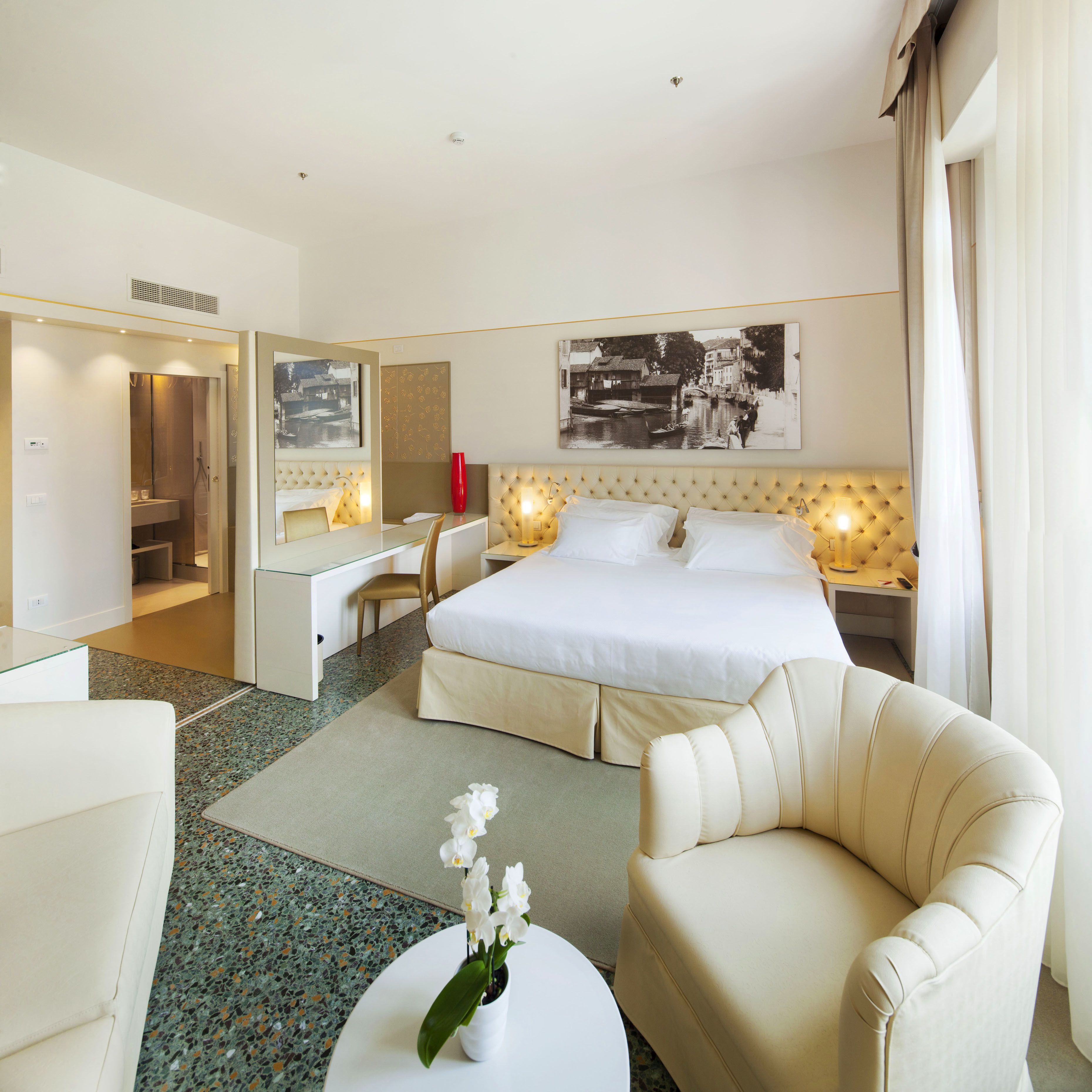 A hotel room with a large bed, a desk, a chair, and a small table with flowers.