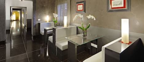 A modern hotel lobby with a glass coffee table, seating area, and framed artwork on the walls.