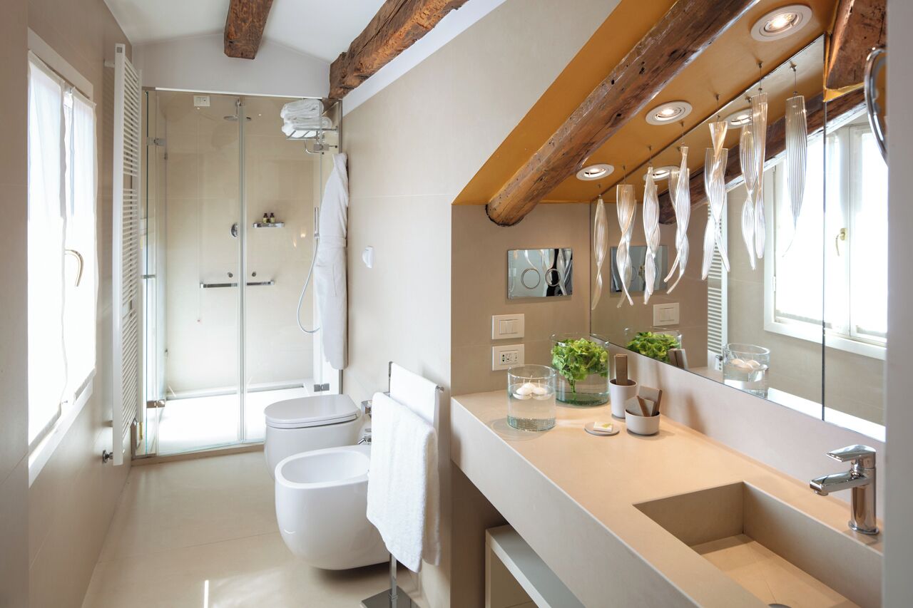 Un baño moderno con ducha envuelta en vidrio, un espejo grande y un tocador color beige con lavamanos.