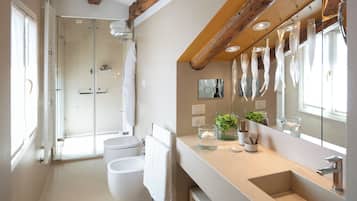 Un baño moderno con ducha envuelta en vidrio, un espejo grande y un tocador color beige con lavamanos.