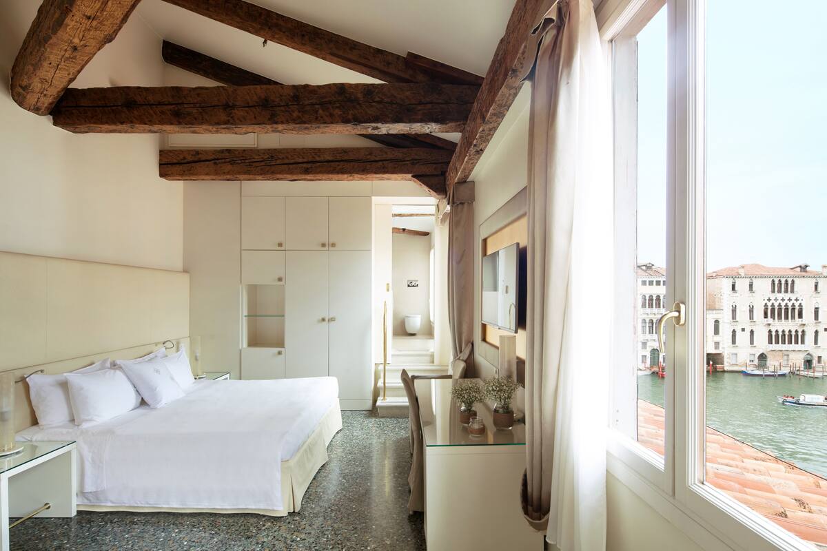 A bedroom with a bed, a desk, and a view of a canal with boats.