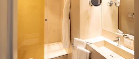 Un baño moderno con ducha de vidrio, lavamanos blanco con espejo y un inodoro.