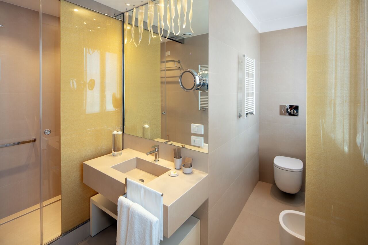 Ein modernes Badezimmer mit Duschkabine aus Glas, großem Spiegel, doppeltem Waschbecken und Toilette.