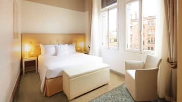 A hotel room with a large bed, bedside lamps, a chair, and a view of buildings through the window.