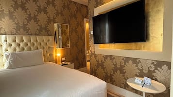 Ein Hotelzimmer mit einem großen Bett, einem an der Wand befestigten Fernseher, einem kleinen Tisch und einem Spiegel.