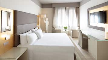 Habitación de hotel moderna con una cama grande, un escritorio, una silla, un televisor y una ventana con cortinas.