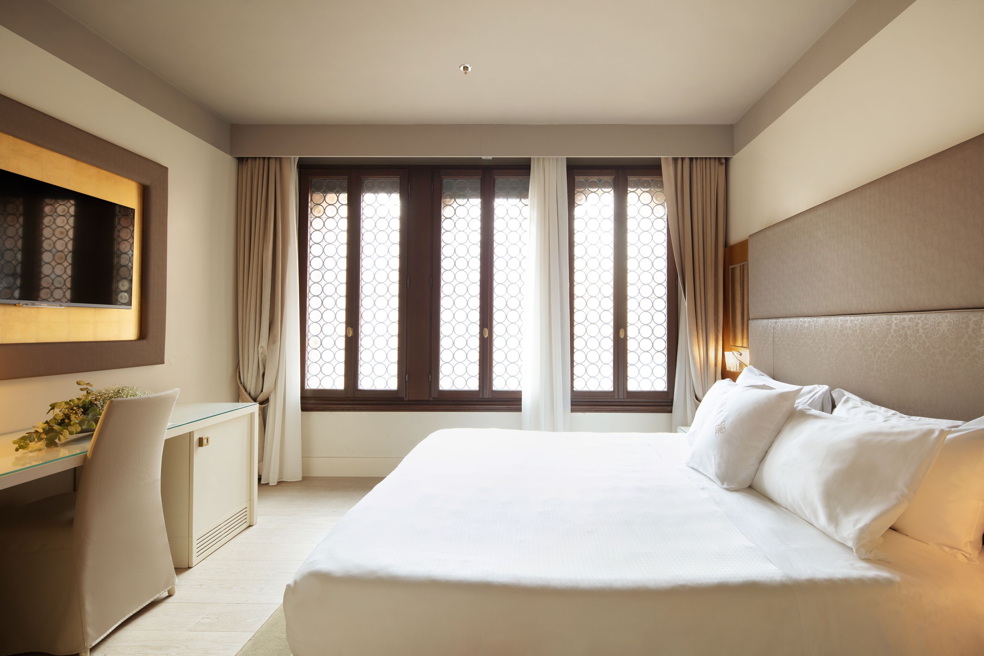 A hotel room with a bed, a desk, a chair, and a TV.
