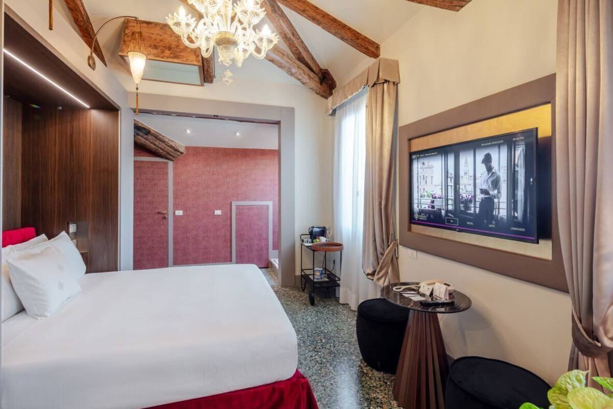 A hotel room with a bed, a television mounted on the wall, a small table, and a chair.
