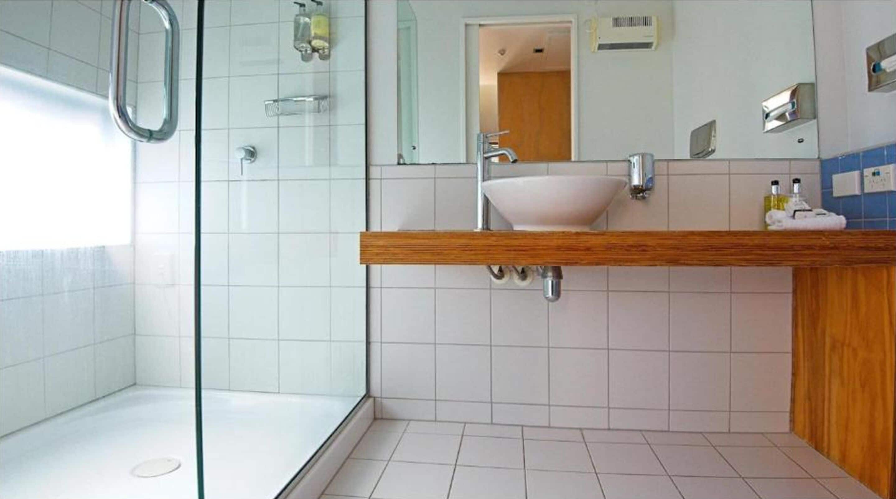 A modern bathroom with a glass shower enclosure, a wooden vanity, and a white sink.