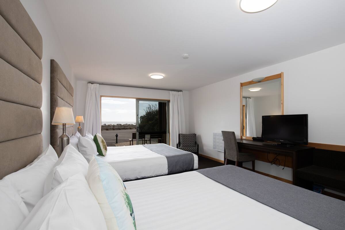 Ein Hotelzimmer mit zwei Betten, einem Schreibtisch, einem Fernseher und Blick ins Freie.