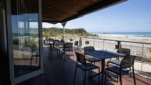 Un espacio al aire libre cubierto con mesas y sillas, con vista a una playa y al océano.