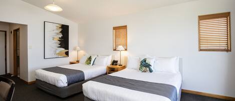 Ett hotellrum med två sängar, ett skrivbord, en stol, en lampa och en tavla på väggen.