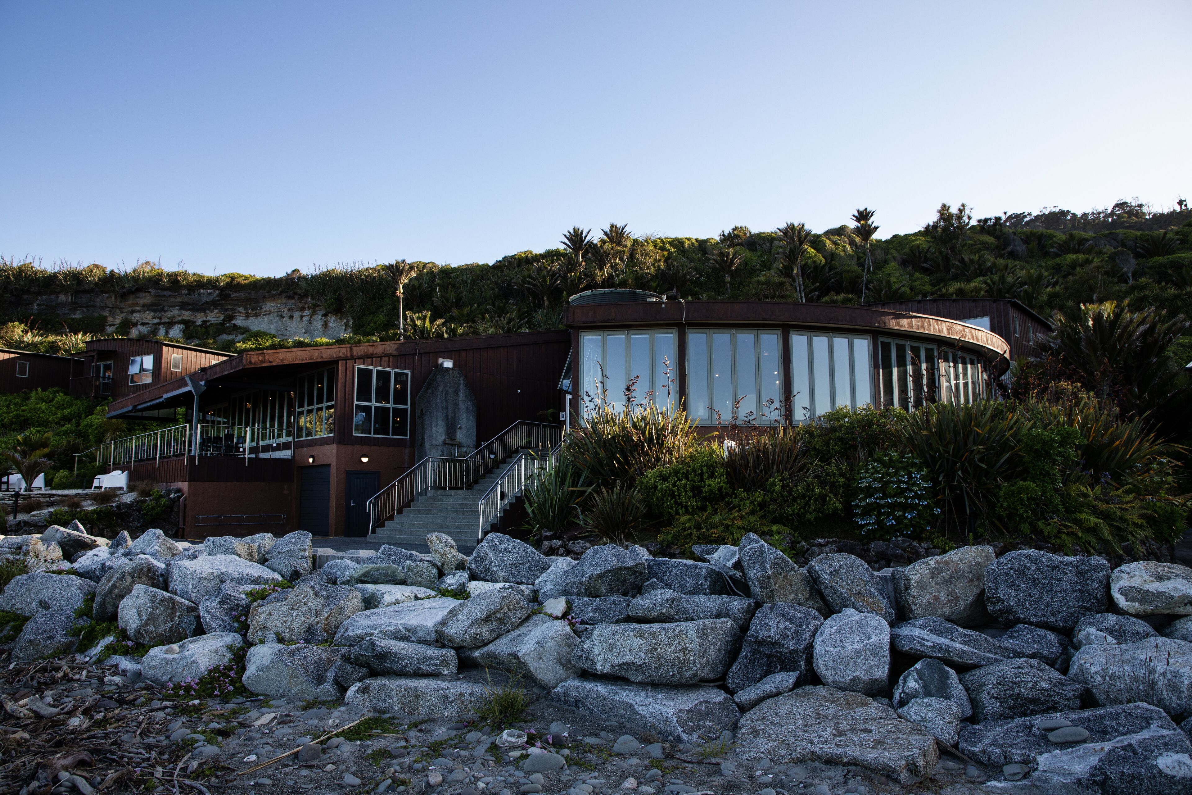 A modern building with a curved glass facade, surrounded by rocks and greenery.