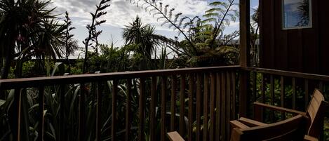 A wooden deck with a chair, surrounded by tropical plants and a wooden railing.