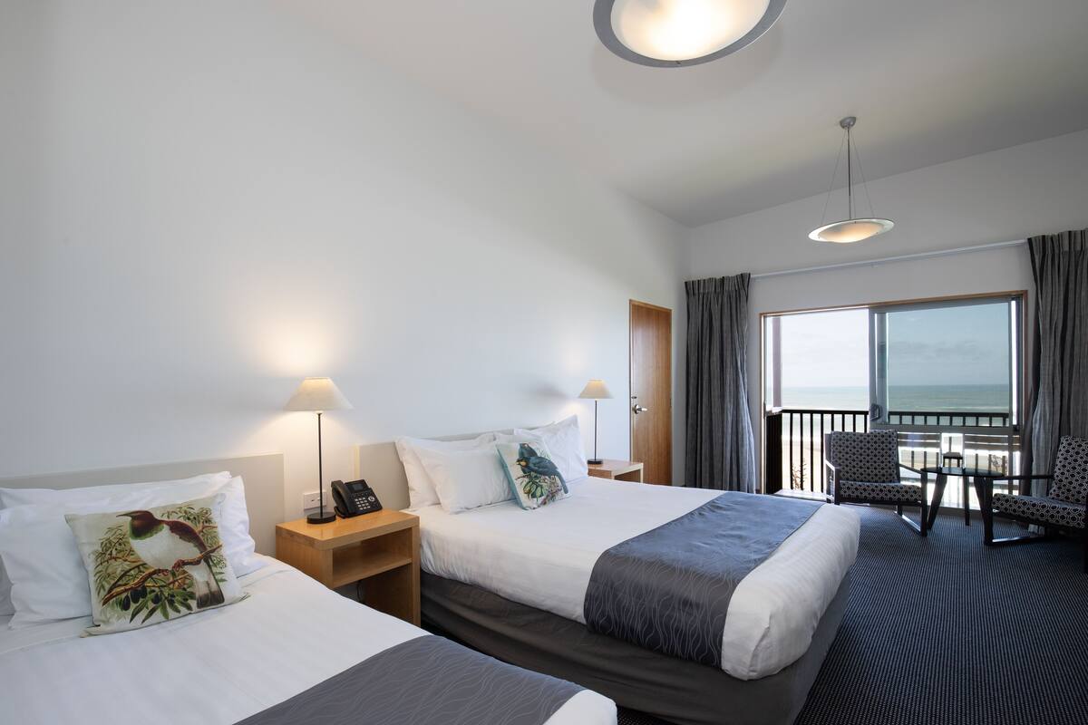 Ein Hotelzimmer mit zwei Betten, einem Balkon mit Tisch und Stühlen und Blick aufs Meer.
