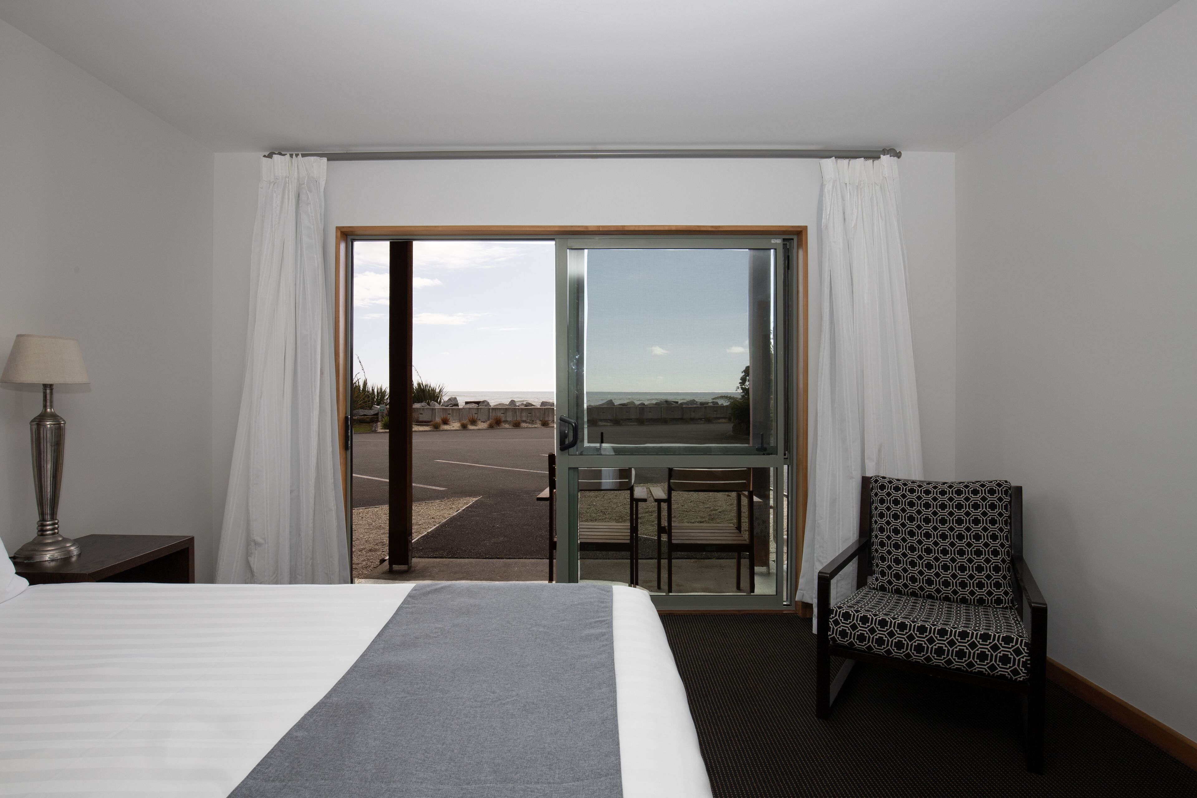 A hotel room with a bed, a chair, a desk, and a view of the outdoors.