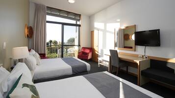Quarto de hotel com duas camas, uma escrivaninha, uma cadeira, televisão e varanda com vista.