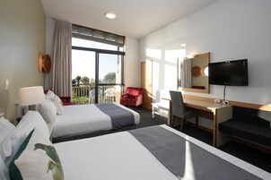 Quarto de hotel com duas camas, uma escrivaninha, uma cadeira, televisão e varanda com vista.