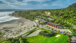 Un resort costero con villas frente a la playa, un camino que lleva a la orilla y abundante vegetación.