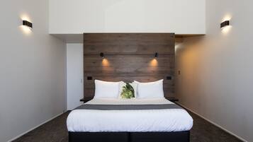 A modern hotel room with a large bed, wooden headboard, and two wall-mounted lights.