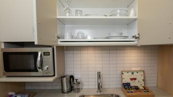 A kitchen with a microwave, a coffee maker, a kettle, and a sink.