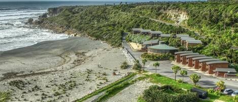 A coastal hotel with multiple buildings, a parking area, and a beach.
