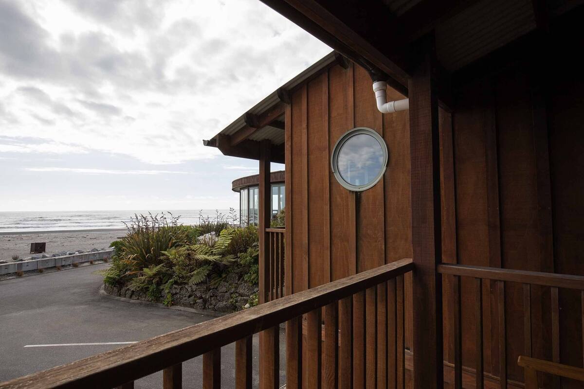 Ein Holzhaus mit einem Balkon mit Blick auf einen Strand.